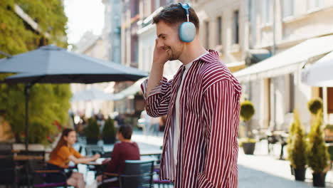 a young man walks down a city street listening to music on his headphones.