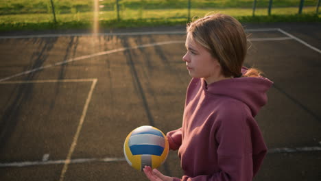 lady in maroon sweater bouncing volleyball in her hand with golden sunlight glow effect, standing on volleyball court with markings and greenery in the background, preparing for the next play