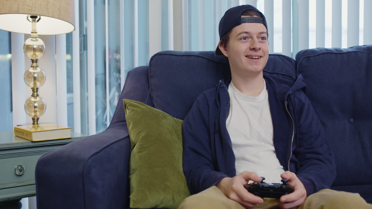 Pria muda bermain video game dengan gembira dan melihat ke samping.