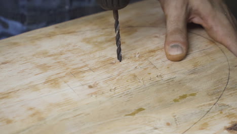 Close-up-of-the-drill-bit-working-on-a-wooden-board-with-male-hand