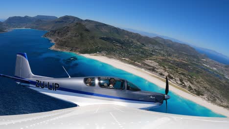 small aeroplane flying over the atlantic ocean with beach and mountains in the background