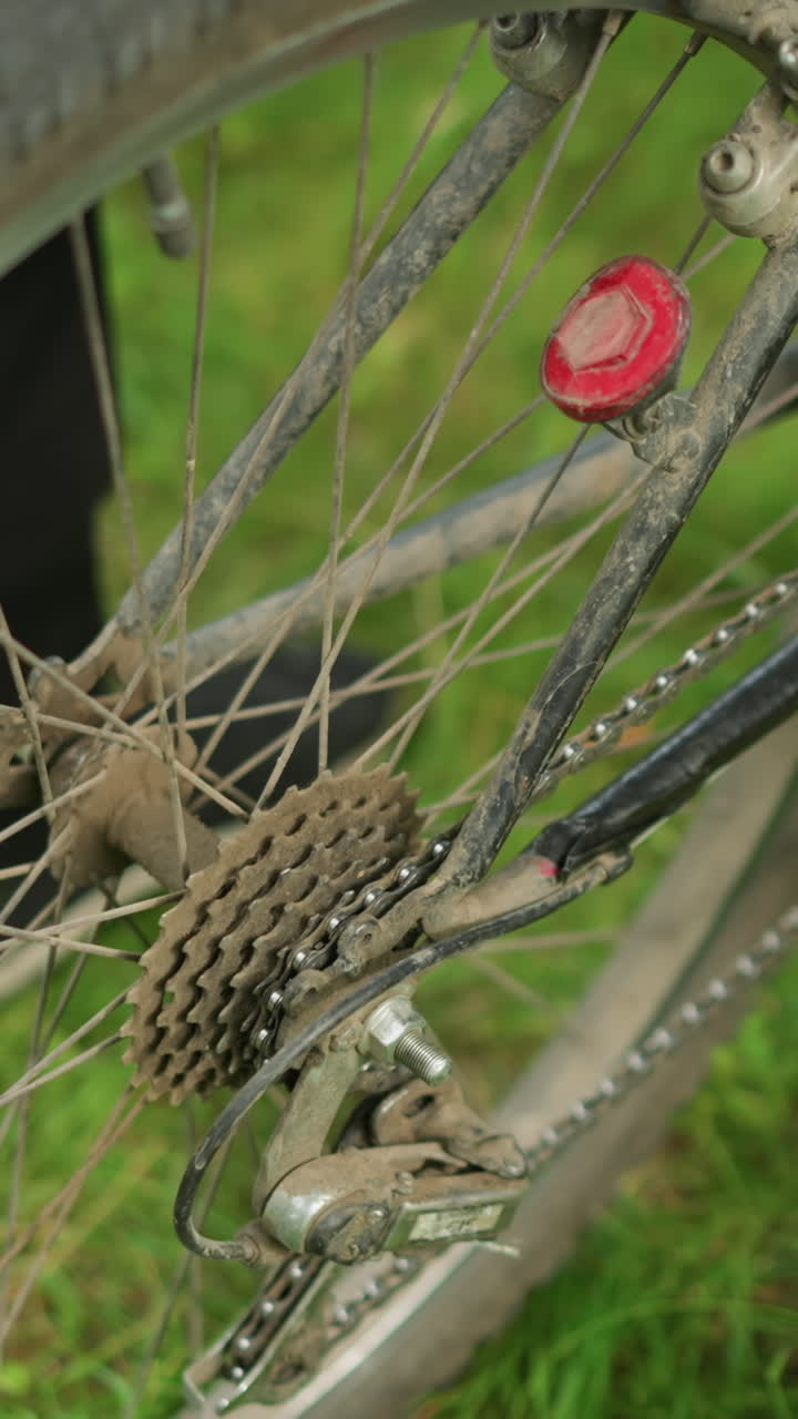 검은색 바지와 운동화를 입은 사람이 잔디에 주차된 자전거 에 서서 뒷 타이어를 들어 올리고 페달을 고 타이어를 회전시켜서 부드럽게 자전거를 내려 놓습니다.