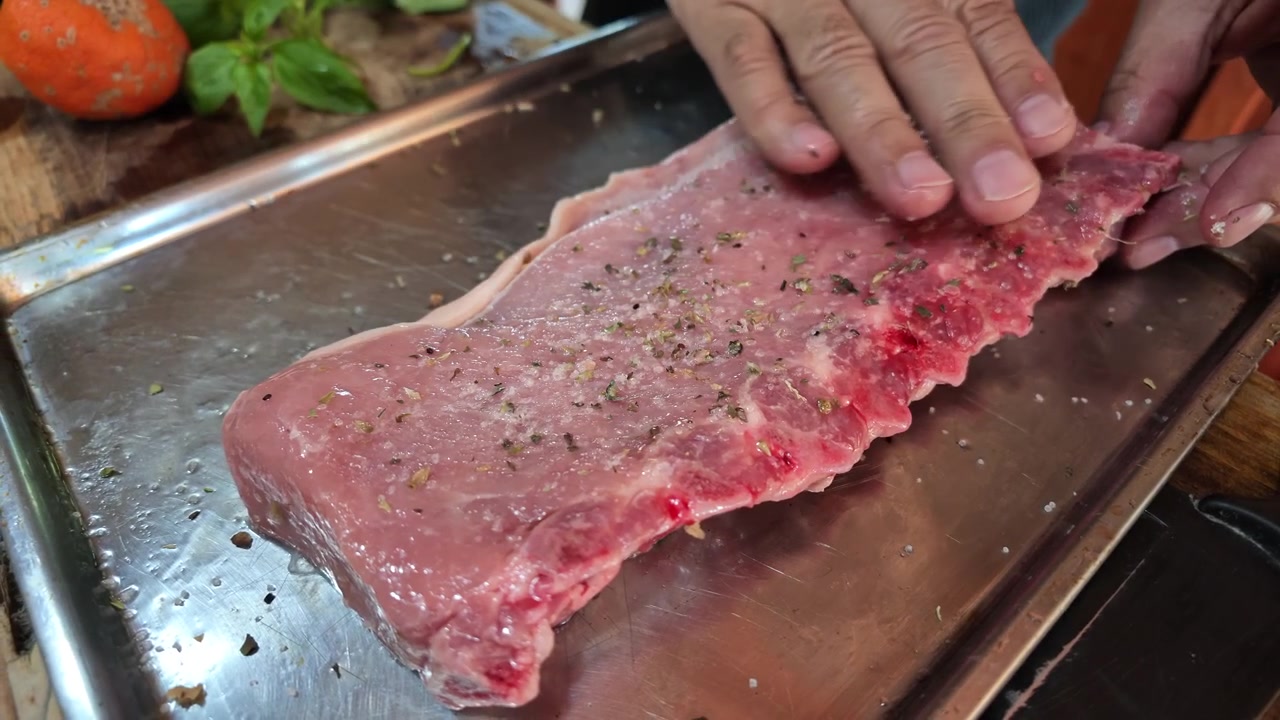 Mani condiscono costine di maiale crude con sale su un vassoio di metallo prima di cuocerle al barbecue