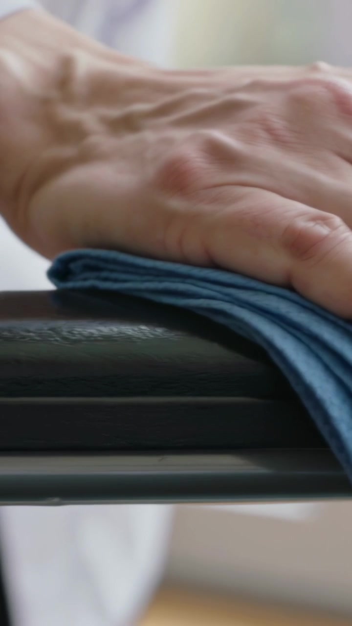 Vertical video: Placing folded blue microfiber cloth hand cuffed wiping black rail in room cleaning