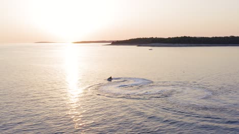 Water-scooter-leaves-S-shaped-wake-on-calm-sea,-clear-sky-golden-hour