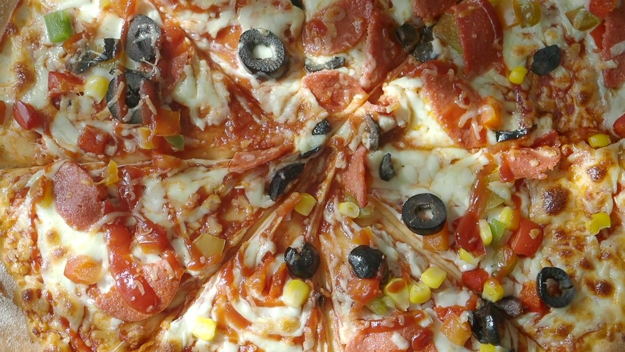 Vista dall'alto di una pizza appena sfornata con salame piccante, olive e verdure.