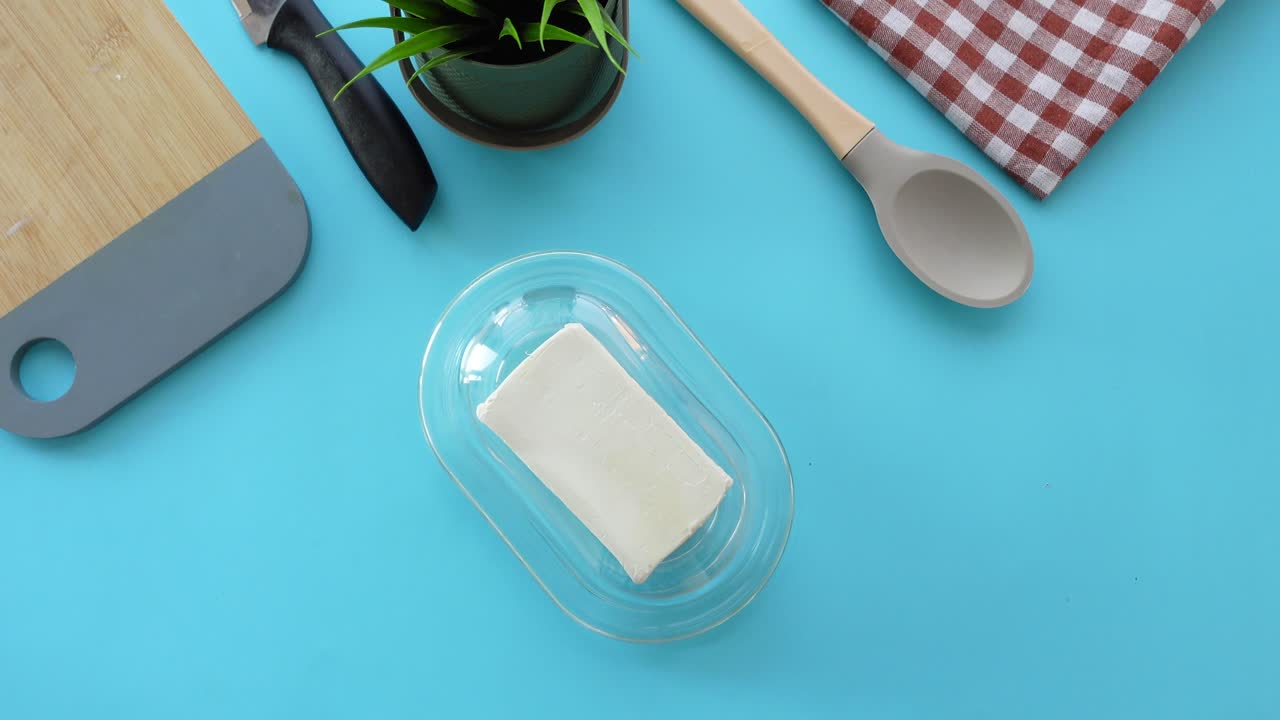 Butter on a butter dish with a knife and a spoon on a blue table