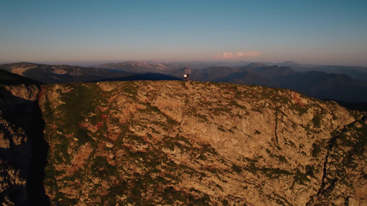 Al tramonto sulle montagne austriache, un duo di avventurieri diventa parte integrante della tela panoramica, con le sfumature eteree mentre si ergono sulle vette, uniti nello stupore sotto i cieli serali