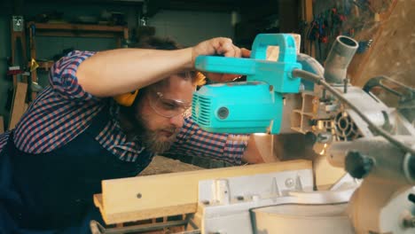 male worker is carefully cutting wood with a circular saw. carpenter in carpentry workshop.