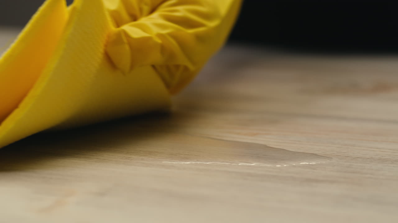 Yellow Sponge Wiping Up Water from Wooden Surface