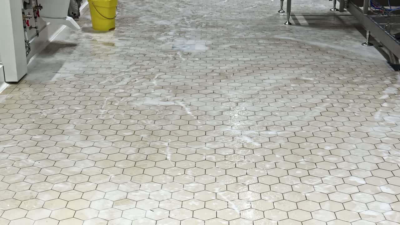 A Wet Hexagon-Tiled Floor is Being Cleaned, with Soap Suds Visible Near a Yellow Bucket - Tilt Shot