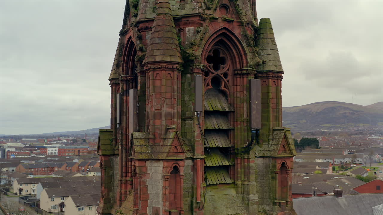 Drone orbit focusing on Carlisle Memorial Church's ornate mid-section, showcasing its weathered stonework and distinctive Gothic arched windows against Belfast's skyline