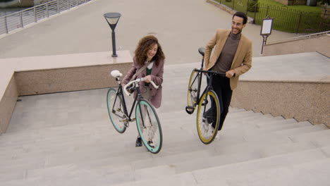 american man and woman in formal clothes carrying their bikes up the stairs while going to work