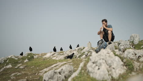 man sitting on the rock eating his sandwich, low perspective, birds surrounding him and waiting for some shared food