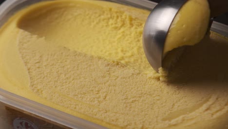 close up view of a person scooping up fresh mango ice cream from tray.