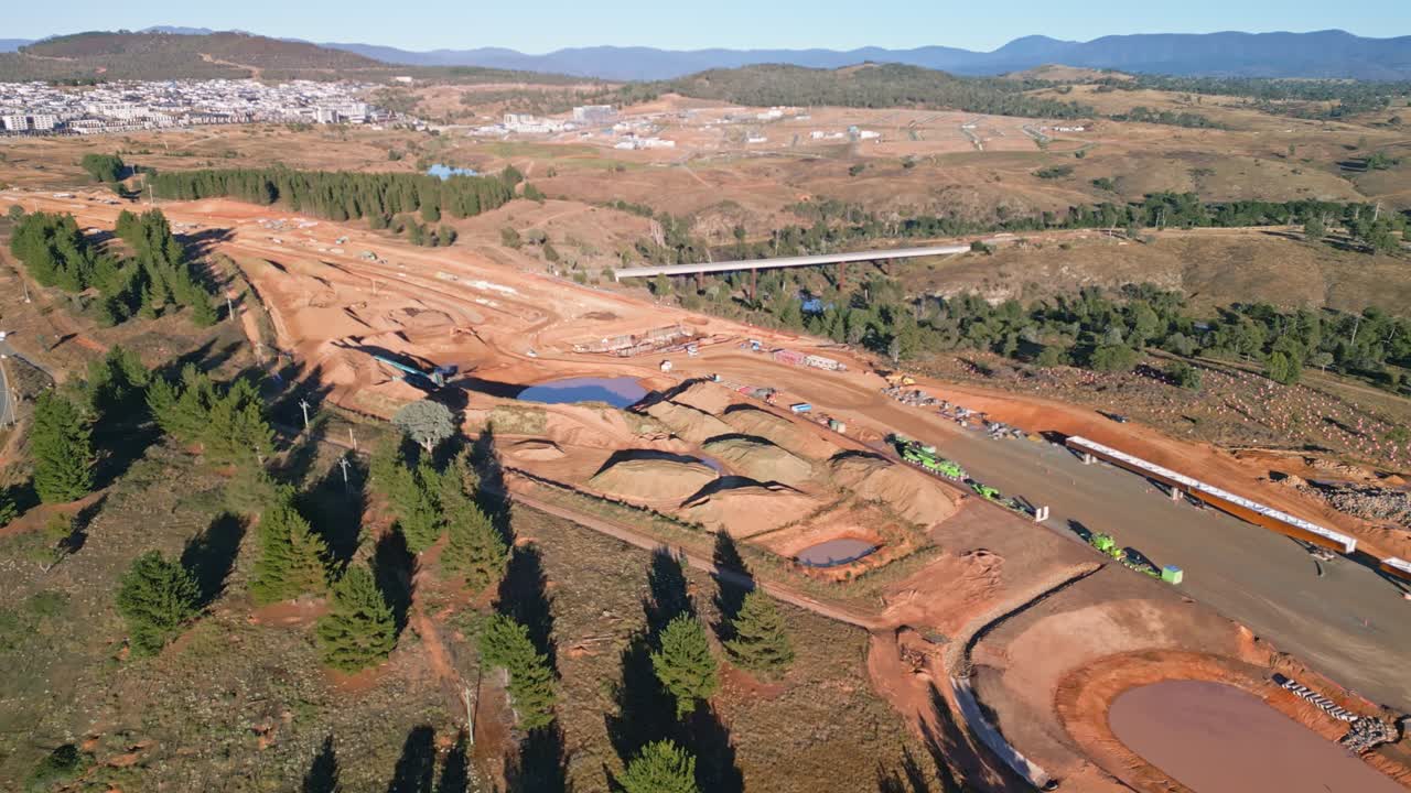 Drone footage shows a small dump truck carrying dirt across an active highway construction area in Canberra.