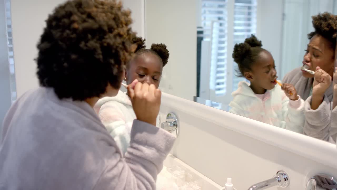 mãe e filha afro-americanas felizes a escovar dentes na casa de banho, câmara lenta.