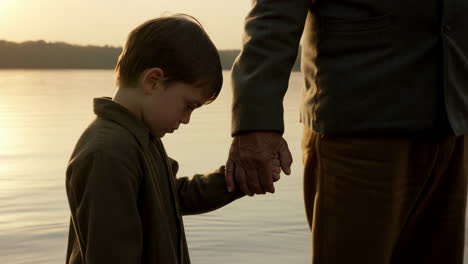 child and adult holding hands by the water at sunset