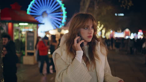 dissatisfied woman talking mobile phone at night amusement park closeup.