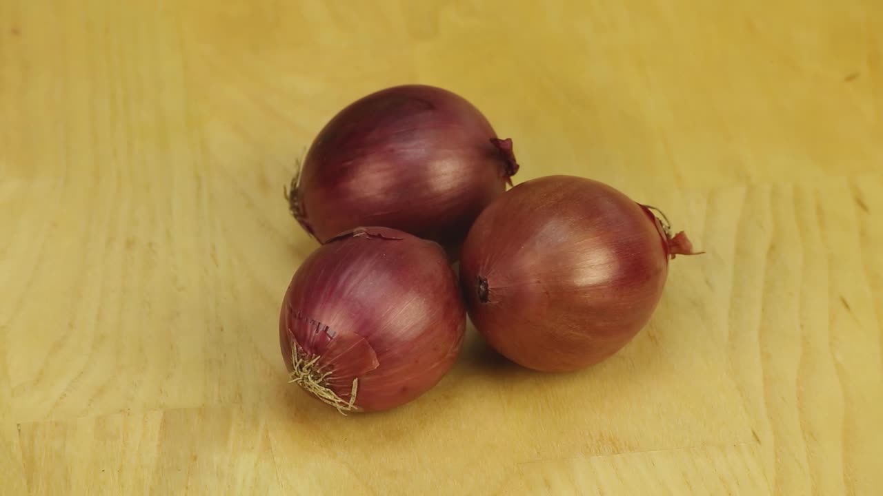 tres cebollas rojas giran en un fondo de tablas de madera