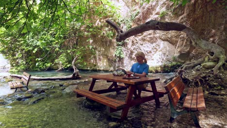 Woman-at-picnic-table-in-river-canyon-setting-drinking-Turkish-chai,-tea