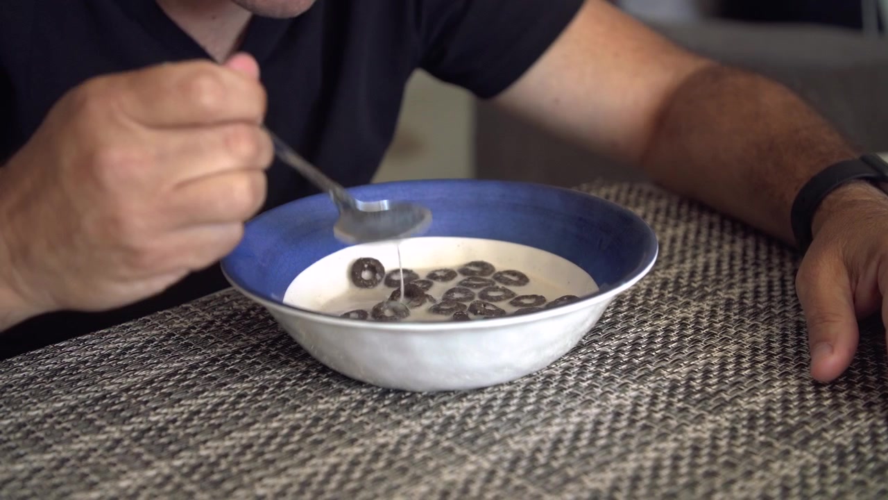Close up insert shot of bowl with cereal and milk. Man takes a spoonful of cereal.