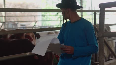 asian male farmer checking on his livestock in the dairy farm and writing notes on clipboard