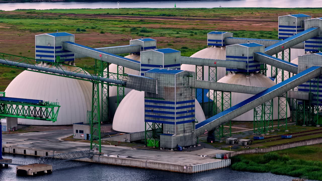 Complex industrial architecture of the Riga Fertilizer Terminal, showing its large dome storage tanks and intricate conveyor belt system for handling chemicals - aerial parallax