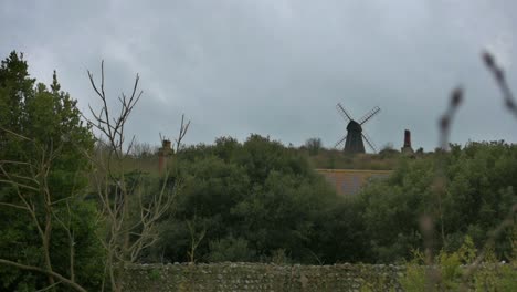 Blick-über-Die-Bäume-Und-Dächer-Auf-Eine-Klassische-Alte-Windmühle,-Die-Auf-Einem-Hügel-Im-Süden-Englands-Thront