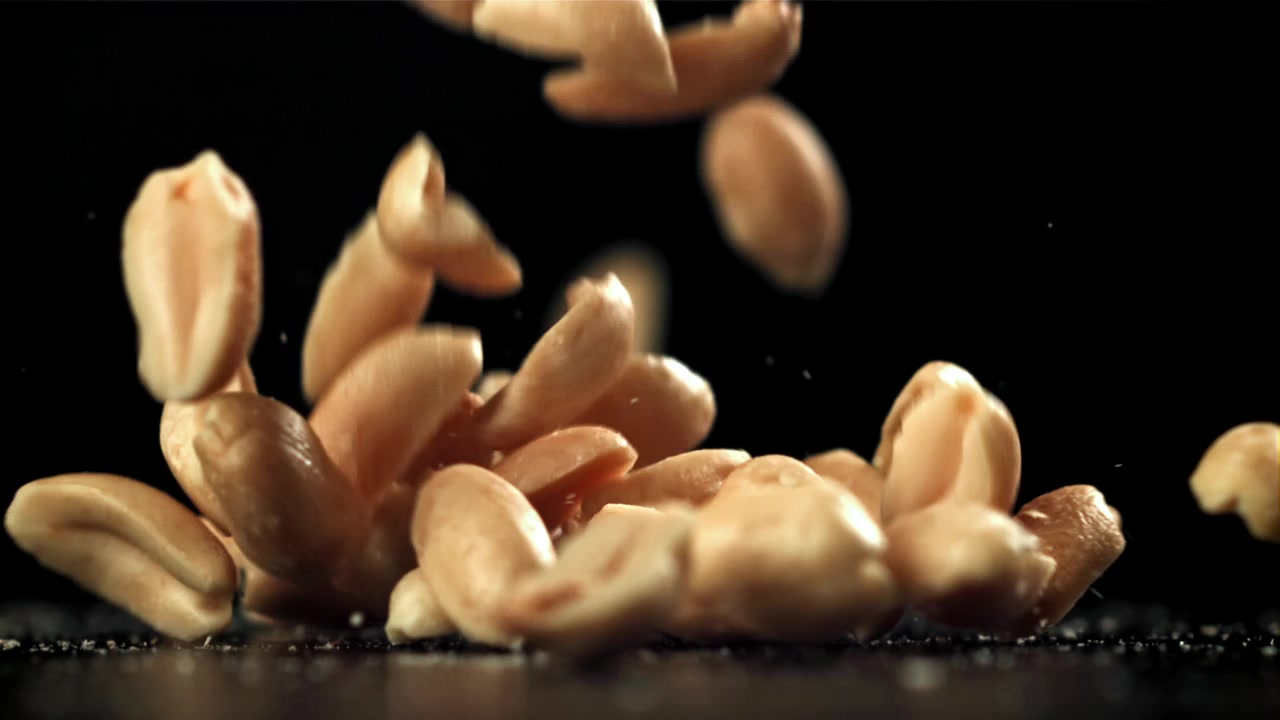 Raw Peanuts Falling in Slow Motion on a Black Background