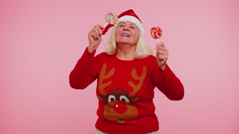 senior grandmother in christmas sweater holding candy striped lollipops dancing making silly faces