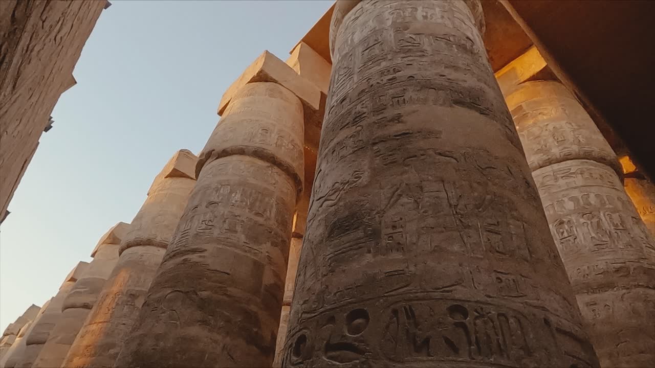Majestic view of the towering stone columns inside the Karnak Temple complex in Luxor, Egypt. The pillars are adorned with intricate hieroglyphic carvings and symbols from ancient Egyptian history.