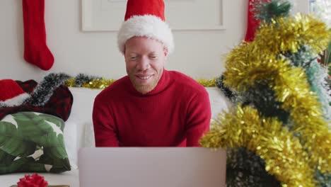 Happy-albino-african-american-man-wearing-santa-hat-making-video-call-at-christmas