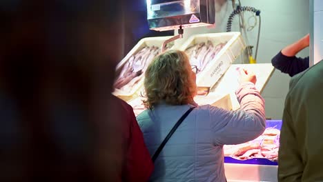 dos mujeres mayores comprando pescado en una pescadería en un mercado local