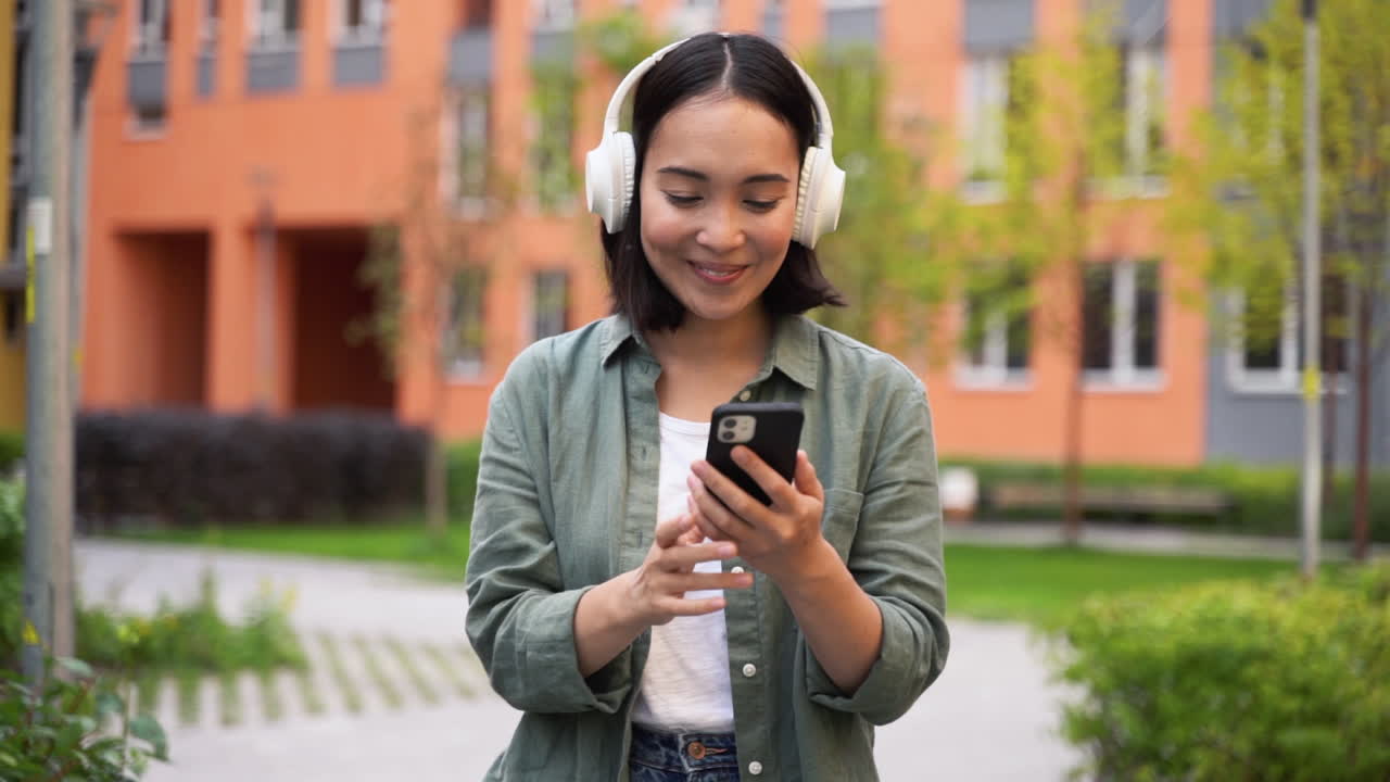 feliz joven japonesa disfrutando de la música en auriculares inalámbricos mientras camina y baila en la calle