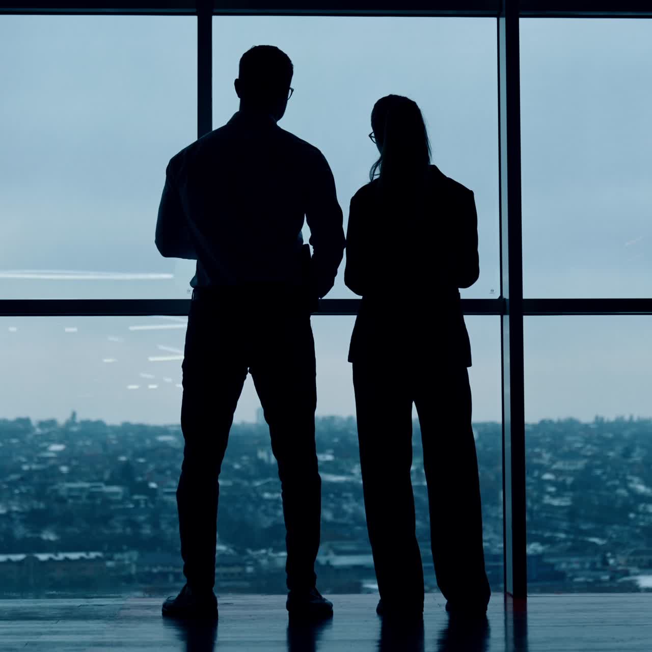 Dark silhouettes of a couple standing looking at the window. Colleagues in office look at cityscape