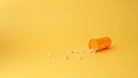 orange pill bottle with spilled white pills on a yellow background