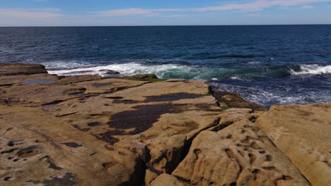 sliding drone shot of rocks being lapped with waves