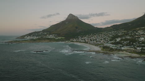 Rückwärts-Fliegen-über-Der-Meeresoberfläche-In-Der-Nähe-Der-Küste.-Blick-Auf-Die-Küstenstadt-Und-Den-Lendenkopfberg.-Kapstadt,-Süd-Afrika