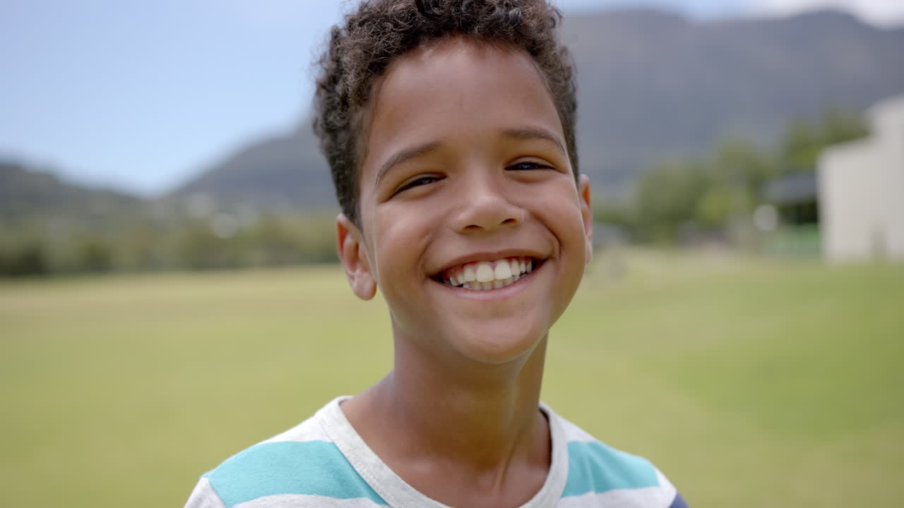Biracial boy with curly hair smiles brightly outdoors