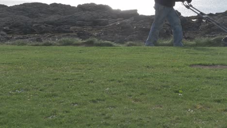 a man with a self-propelled trimmer cuts grass in a lawn near the sea-1