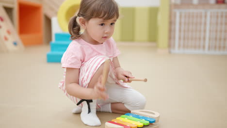 Kleines-Blondes-Kind-Mit-Zöpfen,-Das-Auf-Dem-Xylophon-Spielt-Und-Auf-Dem-Boden-Eines-Indoor-Spielplatzes-Sitzt