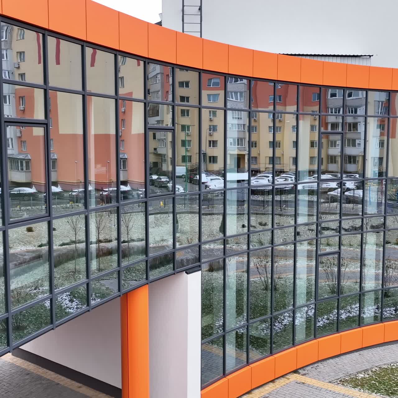 Front passage to the recently-built building with mirror windows and orange design elements. Blocks of flats reflecting in the mirrored windows