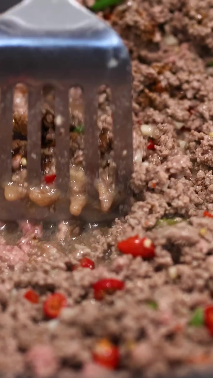 Hackfleisch wird mit Paprika und Soße in einer Küche angebraten. Nahaufnahmen heben den Kochvorgang hervor.