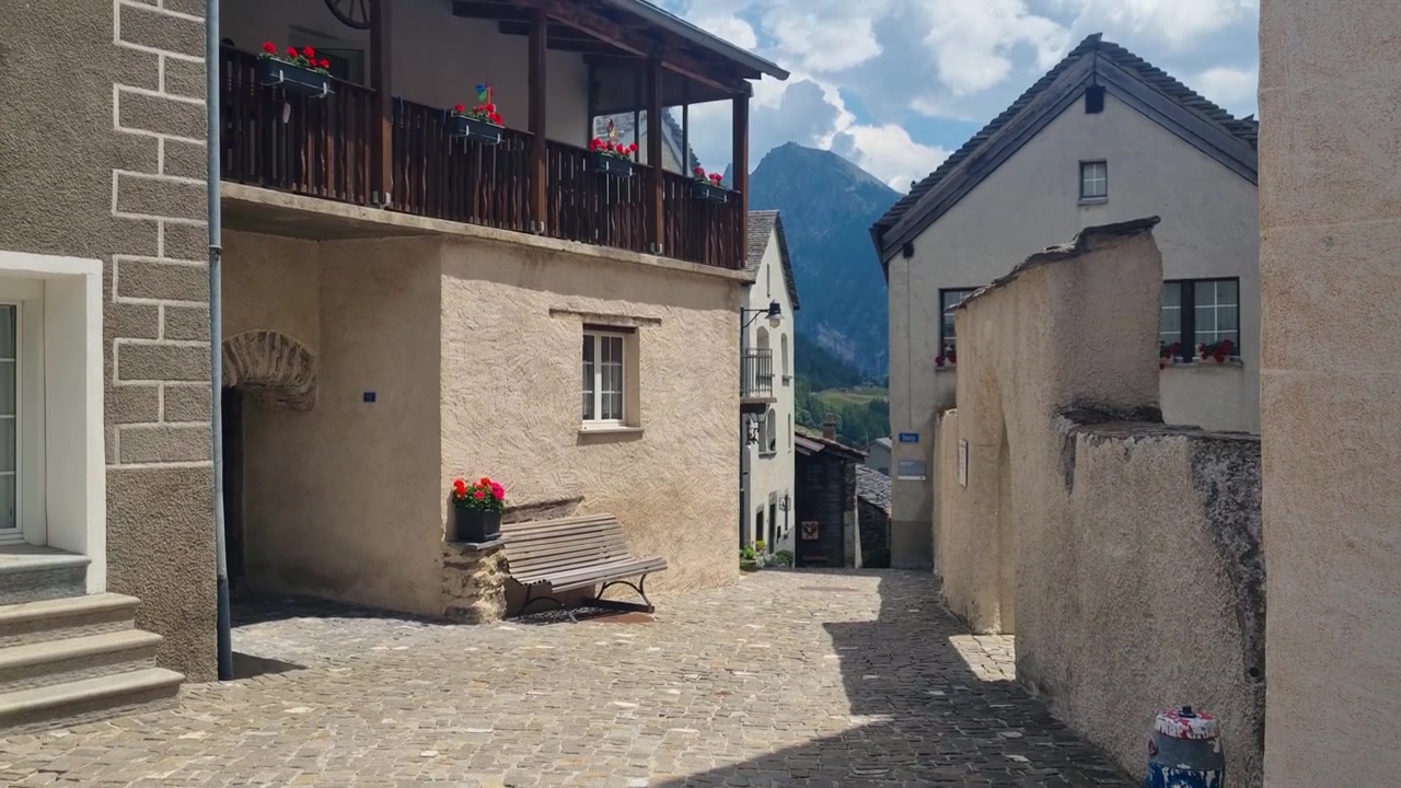 Historic village street in Simplon Dorf, Switzerland, showcasing a narrow cobblestone path, traditional stone houses, and authentic Alpine architecture in a charming mountain setting