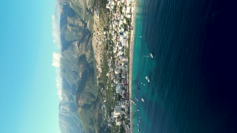 Vertical-shot-of-small-coastal-town-by-the-sea-in-the-south-of-Albania-with-mountains-in-the-background