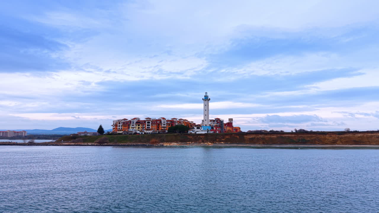 Faro e complesso residenziale su una scogliera a picco sul mare. Veduta aerea di un faro bianco ed edifici dai tetti arancioni su una costa sotto un cielo nuvoloso.