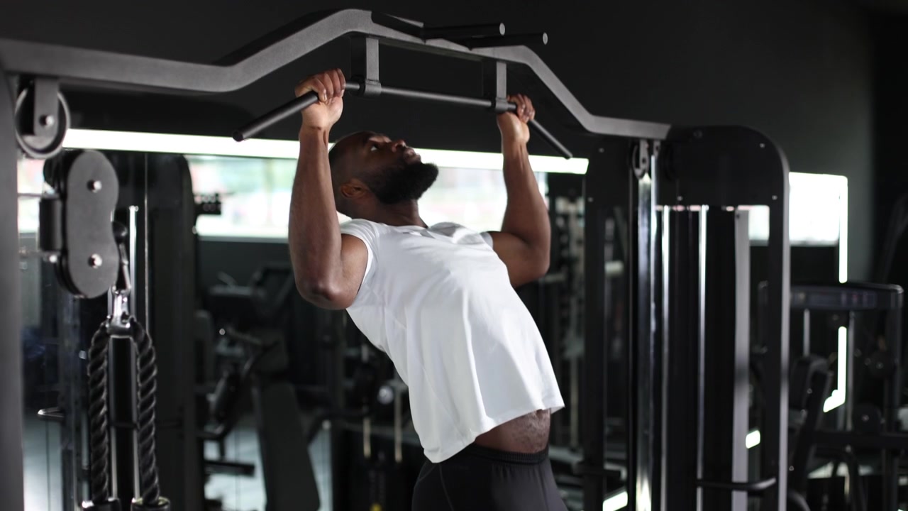 Determined Black Man Doing Pull-Ups in a Modern Gym