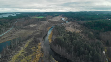 aerial, drone shot, flying over a river surrounded by leafless autumn forest, on a cloudy fall day, in juuka, pohjois-karjala, finland