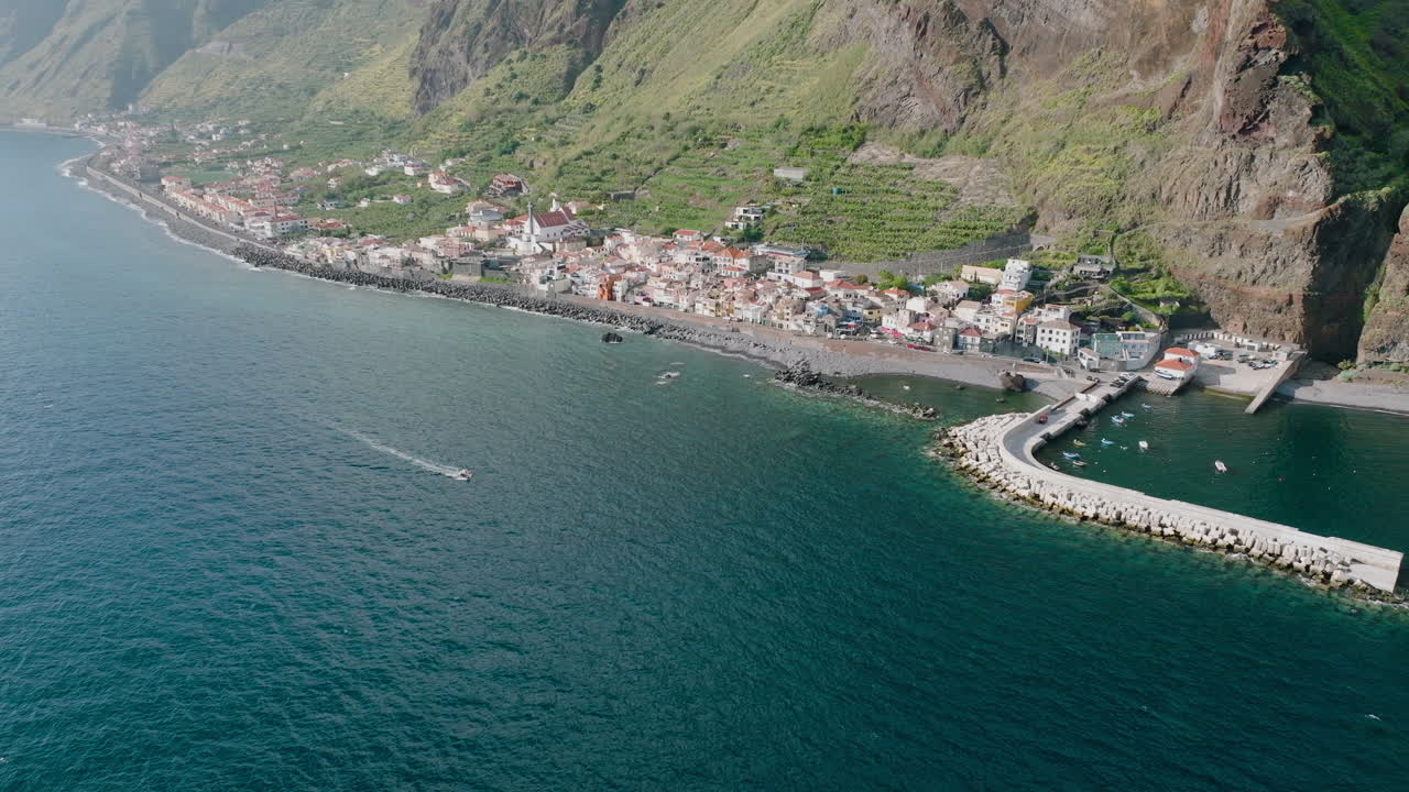 Pueblo costero bajo acantilados, barco navegando hacia el puerto, Madeira